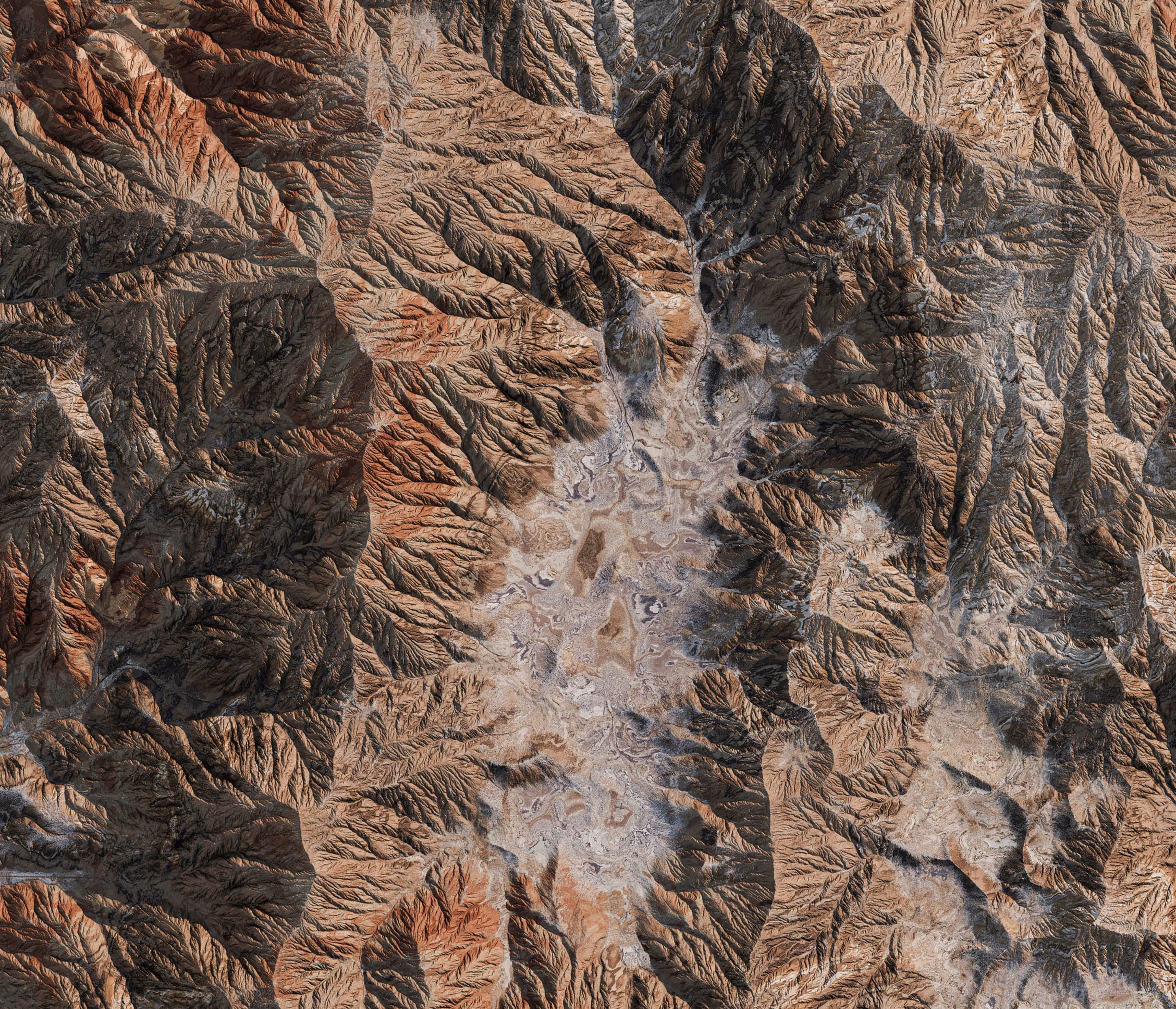 Aerial view of a rugged desert mountain landscape with deep valleys and rocky ridges in varying shades of brown and gray.